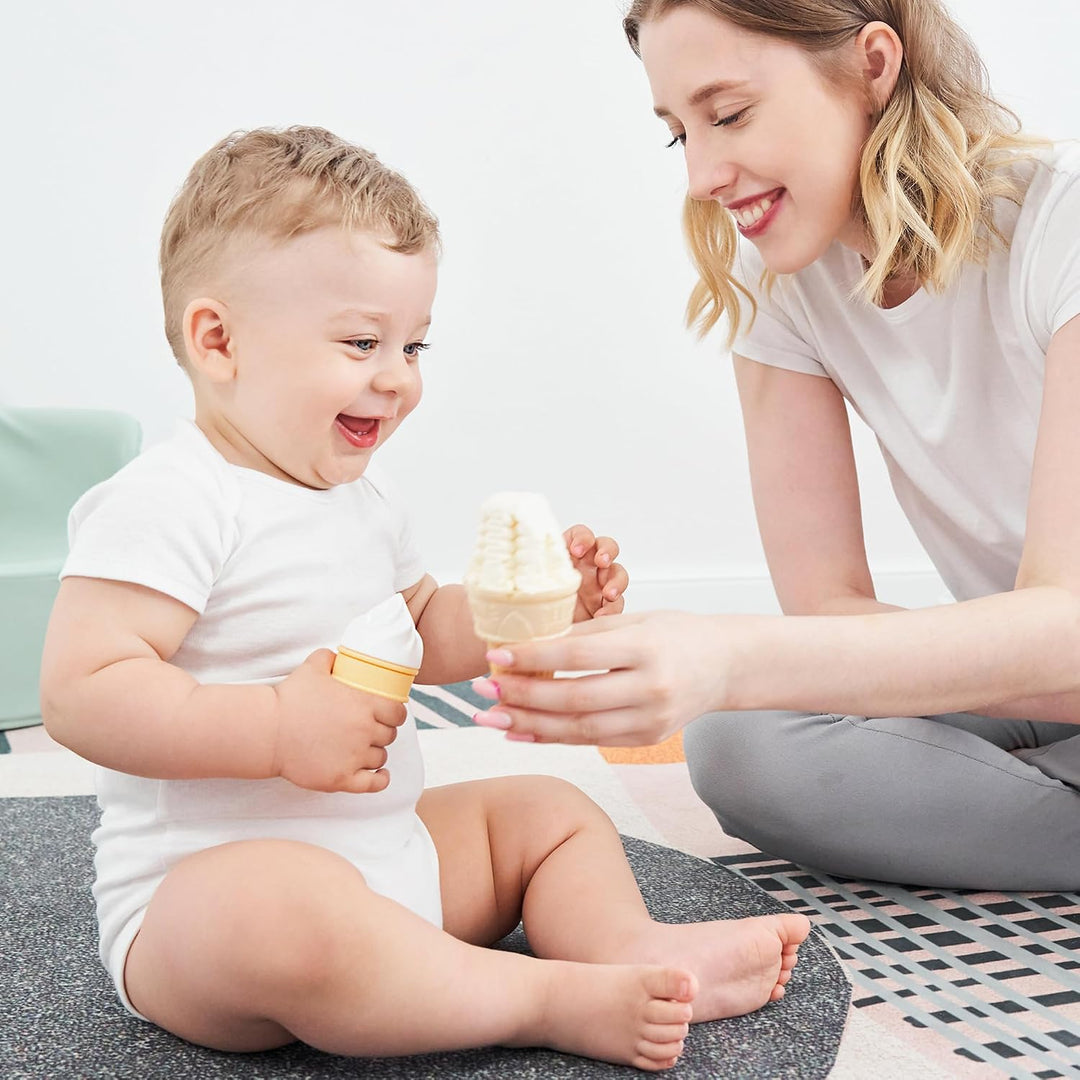 Smiling mother sitting on floor handing Smily Mia ice cream cone teether to laughing baby during playtime showing mother and baby bonding over teething toy