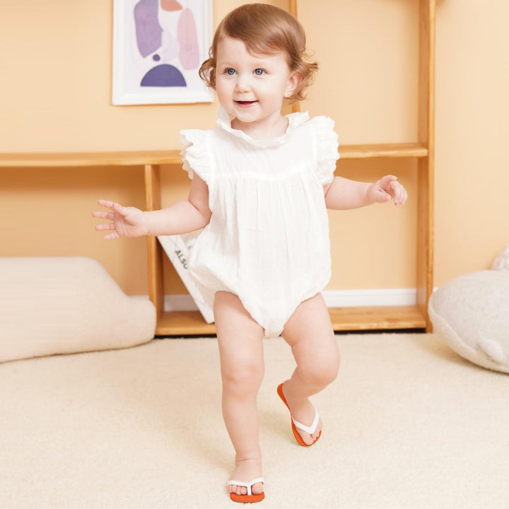 Happy toddler standing and balancing wearing red and white Smily Mia Flip Flop Teether on feet