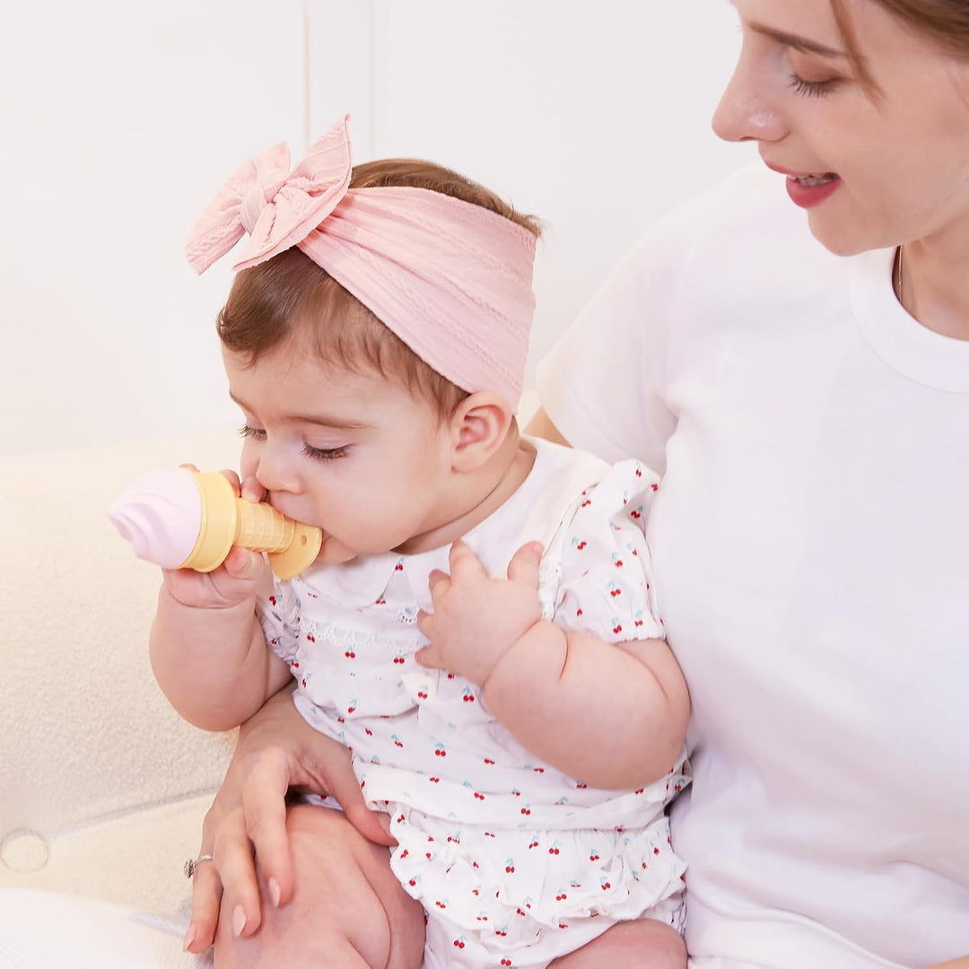 Baby girl in pink bow headband chewing on Smily Mia Pink ice cream cone silicone teether while mom holds her