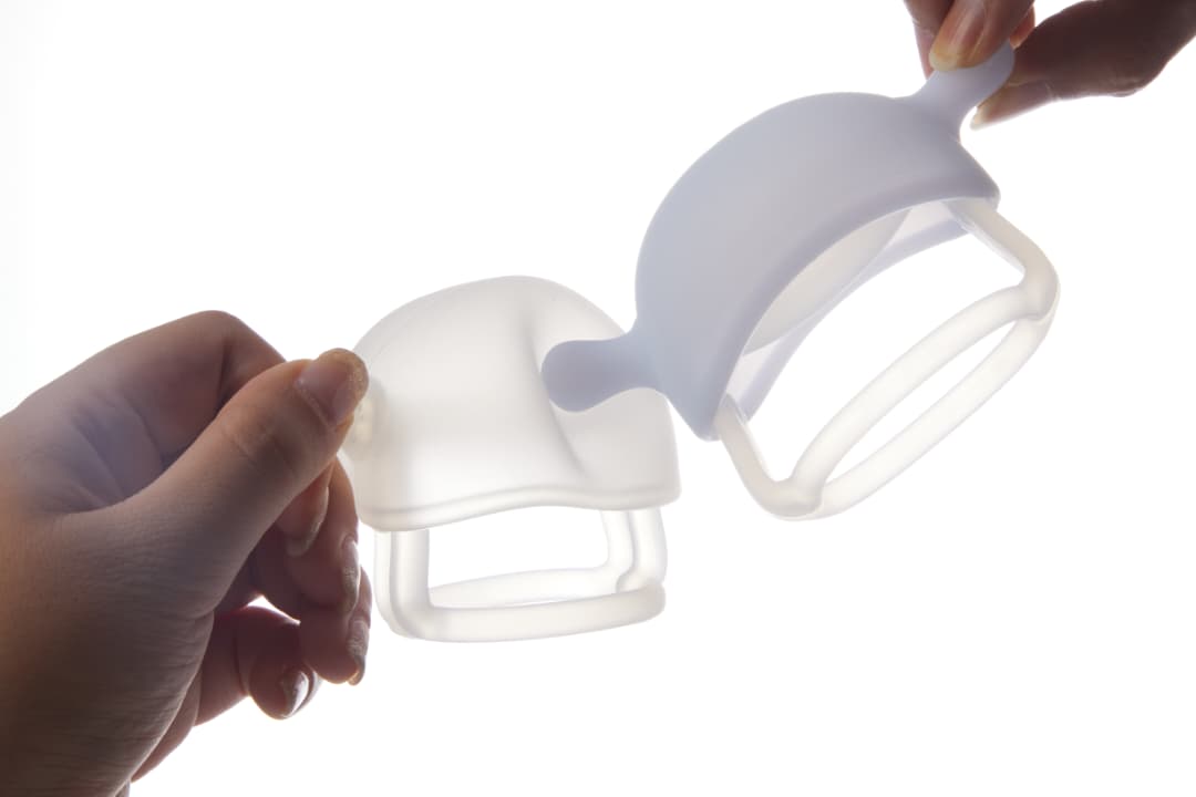 Two hands demonstrating the flexibility and softness of the Smily Mia Mushroom Teething Mitten crystal silicone material showing how the food-grade silicone bends safely without breaking