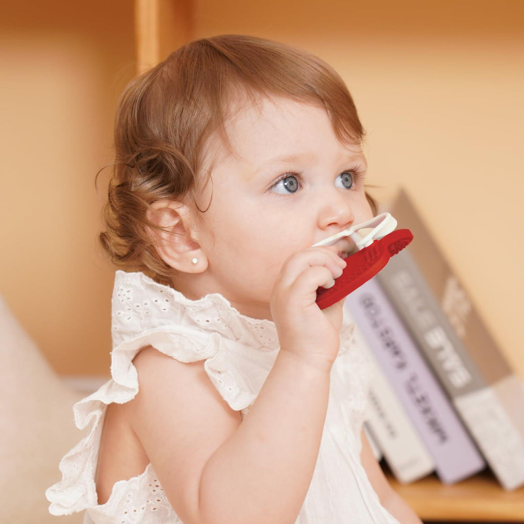 Toddler girl in white dress chewing Smily Mia red Flip-Flop for back gum relief and oral development